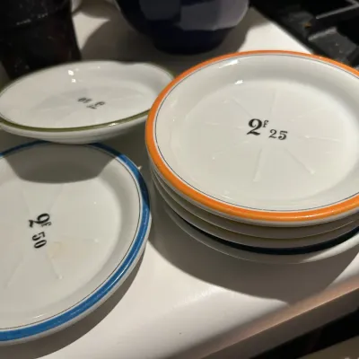 Set of vintage French porcelain bistro coasters featuring hand-painted colored rims and printed franc denominations.