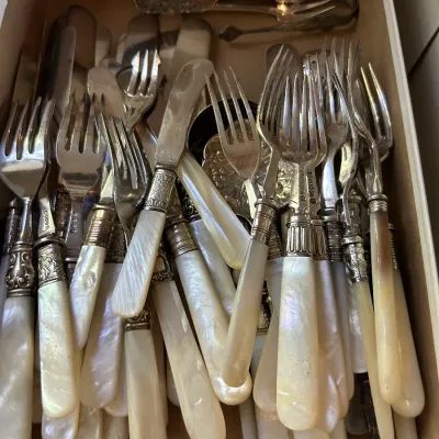 Collection of antique mother-of-pearl handled flatware, including forks and knives with ornate silver-plated collars, stored in a...