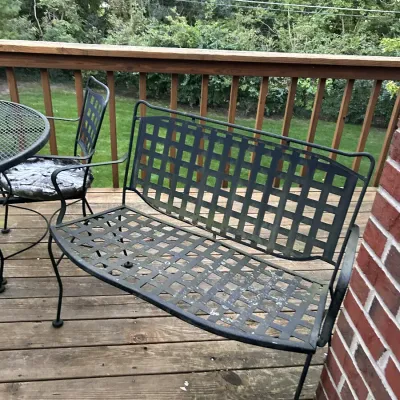 Black wrought iron patio bench with a lattice-style back and seat, showing some weathering from outdoor use.
