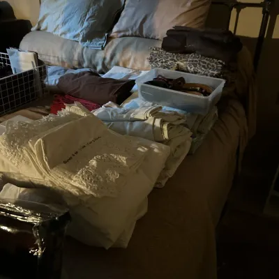 Assorted bed linens, including embroidered white sheets and pillowcases, displayed on a bed alongside storage bins and folded blankets.