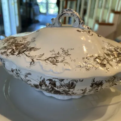 Antique transferware covered tureen with a brown floral pattern on a white glazed ceramic body, featuring an ornate handle and scalloped...