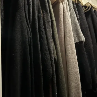 Assortment of knit sweaters and cardigans in neutral tones hanging on a closet rack.