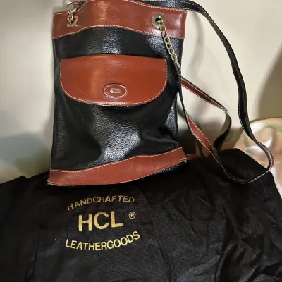 Vintage HCL handcrafted leather bucket bag in black and brown, featuring a front flap pocket, chain-accented shoulder strap, and original...