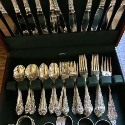 Ornate sterling silver flatware set with highly detailed handles, organized in a green felt-lined wooden storage chest.