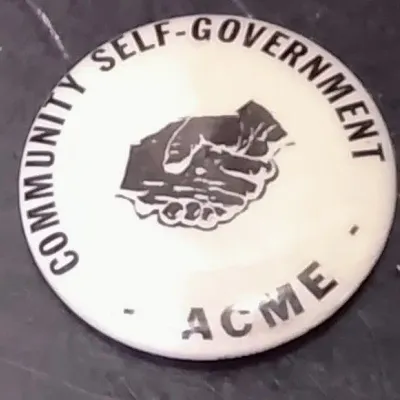 White Pinback Button Featuring The Text "COMMUNITY SELF-GOVERNMENT - ACME" And A Handshake Graphic – Potterville