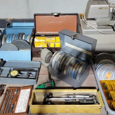 Sale Photo Thumbnail #157: film reels in metal cases, a slide projector, dial indicators, micrometers, and various hand files.