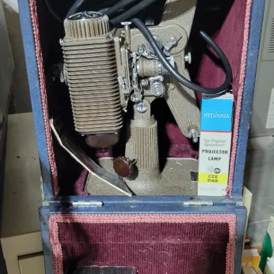 Sale Photo Thumbnail #158: Vintage Revere 8mm movie projector housed in its original case, accompanied by a Sylvania projector lamp box.