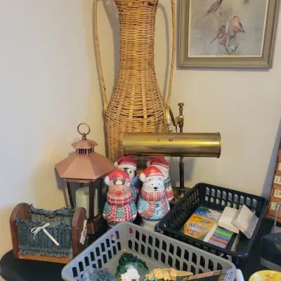 Sale Photo Thumbnail #97: Tall woven wicker floor vase, a brass piano lamp, a copper-finished lantern, and various holiday figurines and craft supplies.