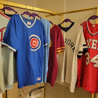 Sale Photo Thumbnail #110: Collection of vintage sports jerseys, including a Chicago Cubs mesh jersey, a New York Knicks jersey, and a Philadelphia 76ers Charles Barkley #34 jersey.