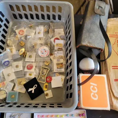 Sale Photo Thumbnail #211: Assortment of vintage collectible pins, a vintage leather case, a baseball, and an Illinois Lead Shot cloth bag.