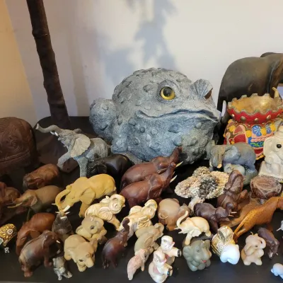 Sale Photo Thumbnail #38: A large collection of decorative elephant figurines in various sizes, materials, and styles, alongside a prominent faux grey stone toad statue.