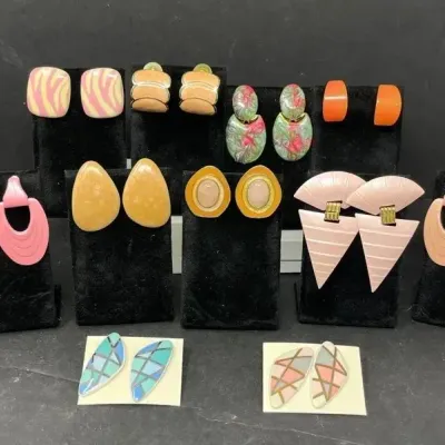Collection of vintage 1980s fashion earrings in various geometric shapes, pastel colors, and enamel finishes, displayed on black velvet...