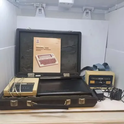 Vintage TRS-80 Model 100 portable computer set, including the technical reference manual, hard carrying case, acoustic coupler modem, and...