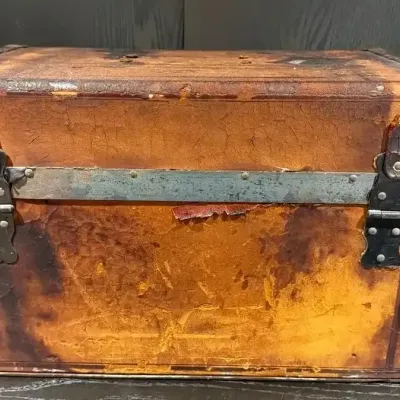 Antique leather-wrapped steamer trunk featuring metal hardware, brass corner guards, and a heavily distressed, weathered patina.