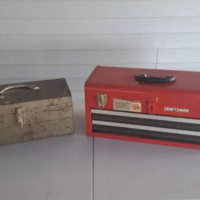Vintage Craftsman red metal three-drawer portable toolbox alongside a smaller, weathered silver-tone metal utility box.