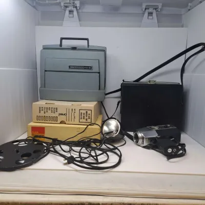 Vintage Kodak Instamatic M85 movie projector, a vintage movie camera with a carrying case, a film reel, and Kodak Ektagraphic boxes.