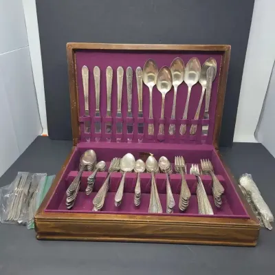 Vintage silver-plated flatware set housed in a wooden storage chest lined with purple felt.