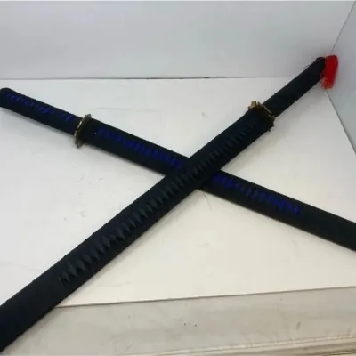 Pair of decorative katana swords in black sheaths with blue and black cord-wrapped handles, crossed on a white surface.
