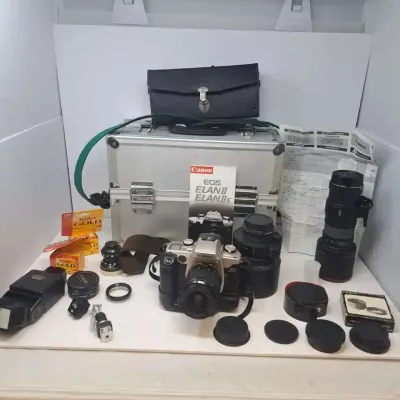 Canon EOS Elan II SLR camera kit, including multiple lenses, a flash unit, filters, Kodak Gold film, manuals, and a silver hard-shell...