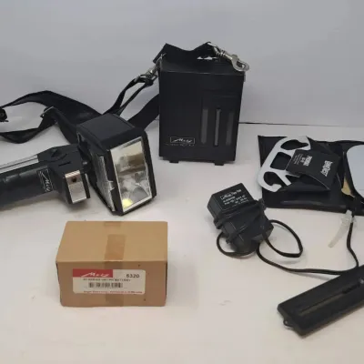 Vintage Metz Mecablitz 45 CT-4 handle-mount flash unit with battery pack, charger, mounting bracket, and accessories.