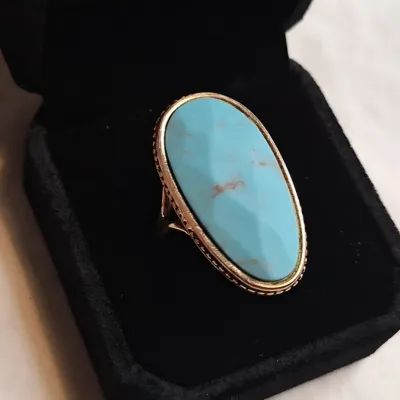 Vintage gold-tone ring featuring a large, elongated oval turquoise cabochon with light matrix, presented in a black velvet jewelry box.