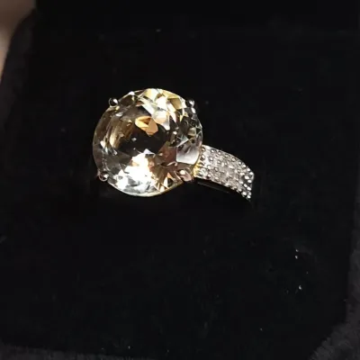 Large round-cut pale yellow gemstone ring set in a textured silver-tone band, presented in a black velvet jewelry box.