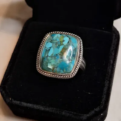 Sterling silver ring featuring a large, rectangular composite turquoise cabochon with a rope-textured border, presented in a black velvet...