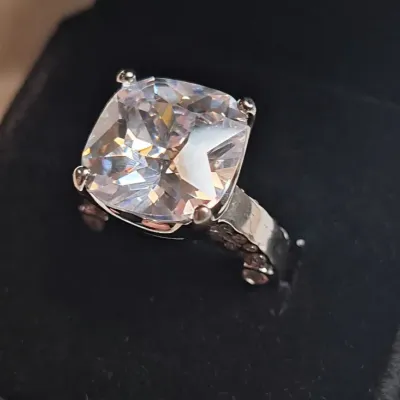 Large cushion-cut cubic zirconia or gemstone ring set in a silver-tone band with accent stones, presented in a black velvet jewelry box.