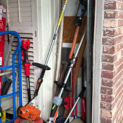 Assorted outdoor power equipment and garden tools, including a Stihl gas-powered string trimmer, a pole saw, and a blue hand truck,...