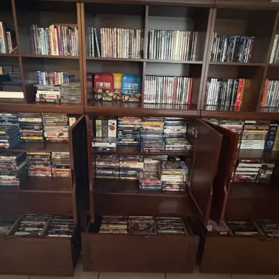 Large dark wood media storage cabinet unit filled with an extensive collection of DVDs, Blu-rays, and box sets, including Star Trek...