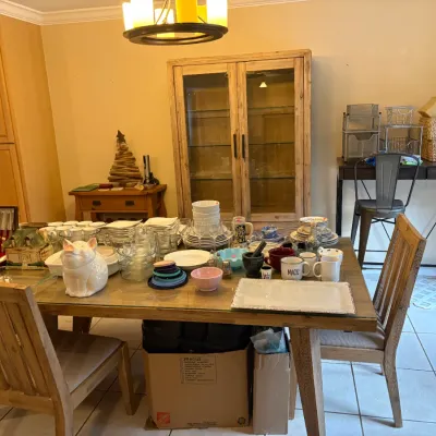 Rustic wooden dining table and chairs set, featuring a glass top and displayed with various kitchenware, tableware, and a ceramic pig...