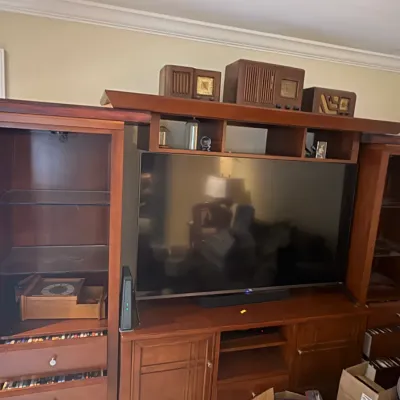 Large cherry-finished wooden entertainment center with glass shelving, drawers, and cabinet storage, shown holding a flat-screen...