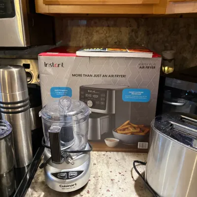 Cuisinart Mini-Prep Plus food processor in brushed chrome, shown alongside a boxed Instant Vortex Plus air fryer and a stainless steel...