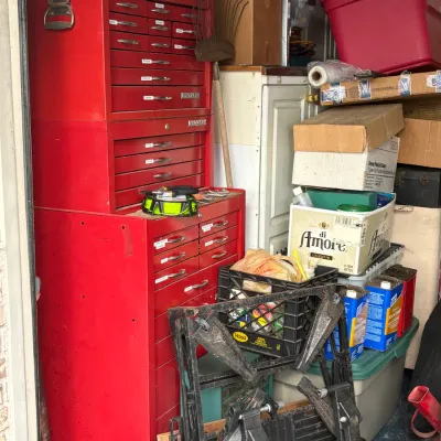 Vintage red metal rolling tool chest and top box, surrounded by various garage items including a folding work table, storage bins, and...