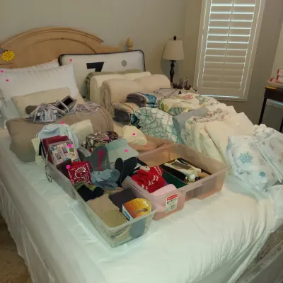 Sale Photo Thumbnail #18: Assorted bedding, linens, and accessories displayed on a bed, including blankets, pillows, and plastic storage bins filled with small items.