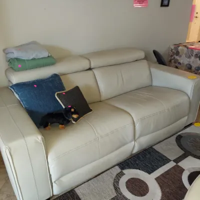Sale Photo Thumbnail #5: Modern off-white leather sofa with adjustable headrests, styled with throw pillows and a plush toy, sitting on a geometric patterned area rug.