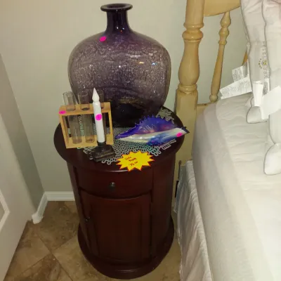 Sale Photo Thumbnail #17: Round dark wood nightstand with a single drawer and cabinet door, styled with a large purple glass vase, a decorative glass dish, and a small test tube rack.