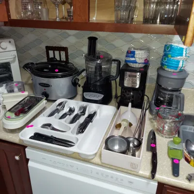Sale Photo Thumbnail #8: Assorted kitchen appliances and utensils, including a Hamilton Beach slow cooker, a food processor, two coffee makers, a flatware organizer with utensils, and various glassware.