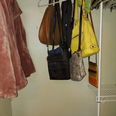 Sale Photo Thumbnail #16: Assorted women's handbags and purses hanging in a closet, including a yellow leather shoulder bag, a brown leather hobo bag, and a black crossbody bag.