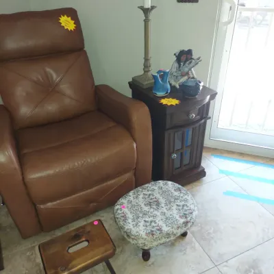 Sale Photo Thumbnail #3: Brown leather recliner paired with a dark wood side table, a tall buffet lamp, a floral upholstered footstool, and a small wooden step stool.