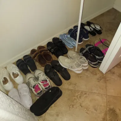 Sale Photo Thumbnail #15: Assortment of women's shoes, including athletic sneakers, sandals, and slides, lined up on a tiled floor.