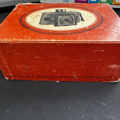 Sale Photo Thumbnail #66: Vintage red Agfa Ansco camera box showing wear on the edges, with a graphic of a camera on the lid.