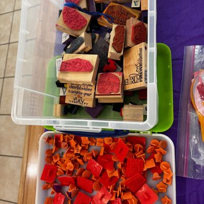Assortment of crafting rubber stamps, including wood-mounted stamps in a clear plastic bin and a collection of small orange and red...