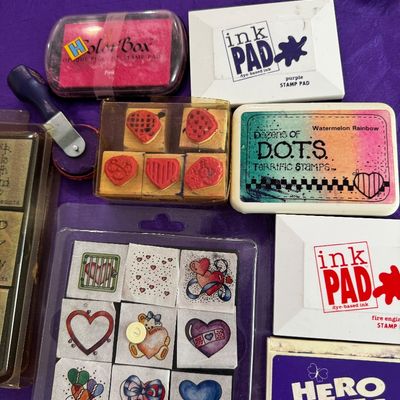 Assortment of vintage rubber stamps and ink pads, including a set of heart-themed stamps, a ColorBox pink pigment pad, and a Hero Arts...