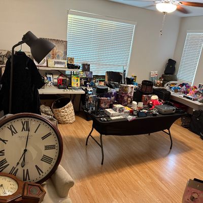 Living room filled with sale items including a large Sterling & Noble wall clock, folding tables with collectibles, electronics, and...