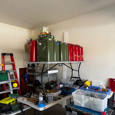 Sale Photo Thumbnail #77: Assorted garage items including a row of metal jerry cans in red and olive drab, various plastic storage bins, hand tools, and a Husky rolling tool box.