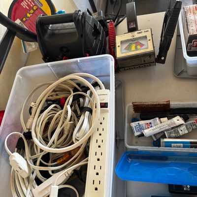 Assorted garage and electrical items, including a plastic bin filled with extension cords and a RadioShack power strip, alongside an OTC...