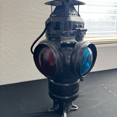 Sale Photo Thumbnail #18: Vintage black metal railroad switch lantern featuring red and blue glass lenses, mounted on a small stand.