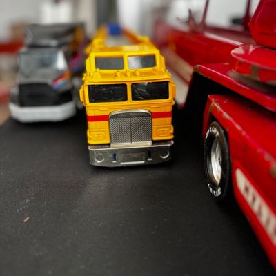 Sale Photo Thumbnail #38: Vintage toy semi-trucks, including a yellow cabover model and a red fire truck, showing some wear from play.