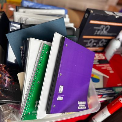 Assorted school and office supplies, including spiral notebooks, three-ring binders, and folders in a clear plastic storage bin.